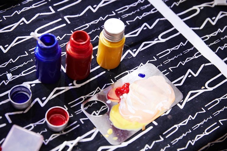 Three bottles of makeup paint in blue, red and yellow on a MAC cosmetics piece of fabric