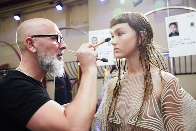 A makeup artist applying makeup on a model backstage at Iris Van Herpen's 10th Anniversary Fashion S...