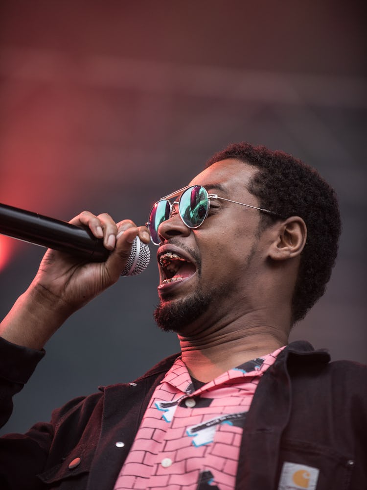 Danny Brown with a microphone performing in a brown jacket and pink shirt at the Pitchfork Music Fes...