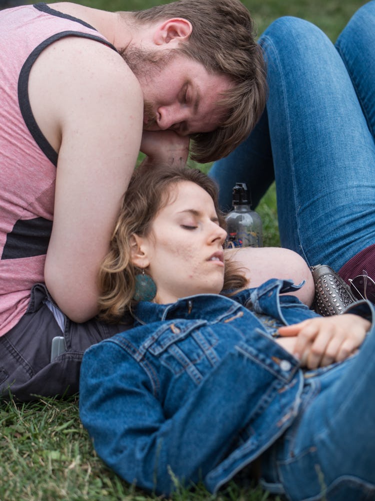A woman in a blue denim jacket lying on grass and a man in a pink shirt sitting next to her at the P...