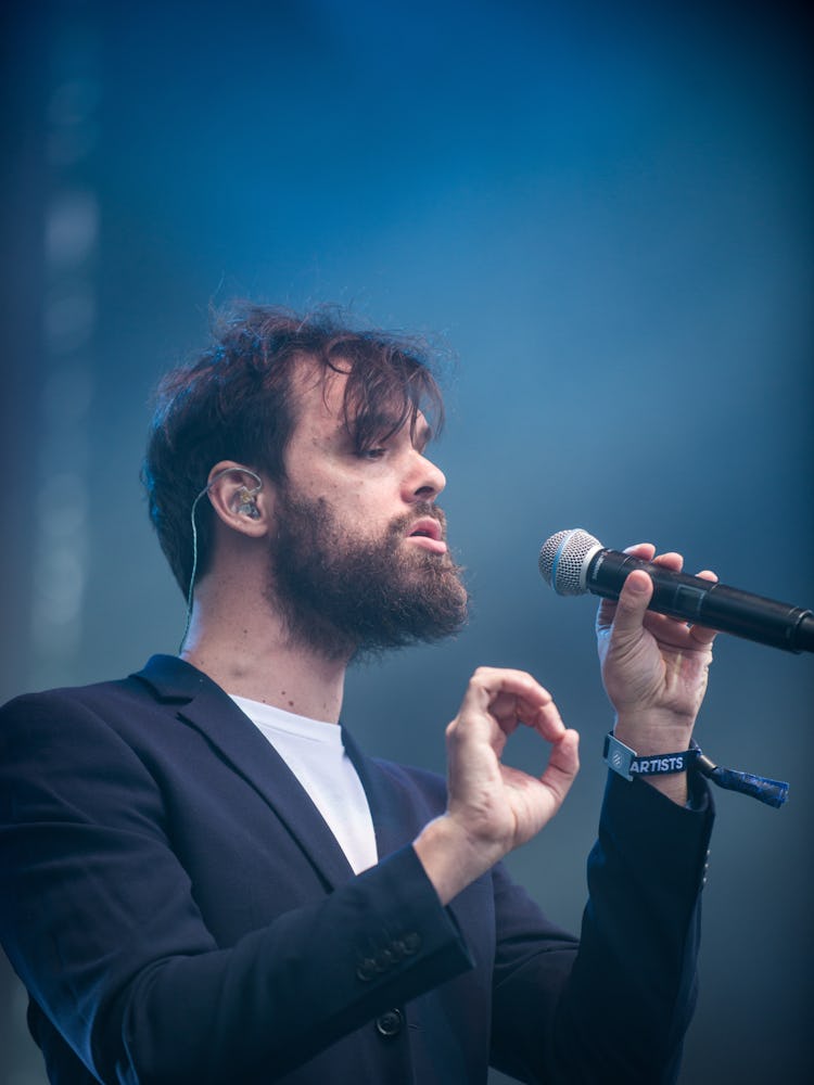 A bearded man in a white shirt and a black blazer performing with a microphone at the Pitchfork Musi...