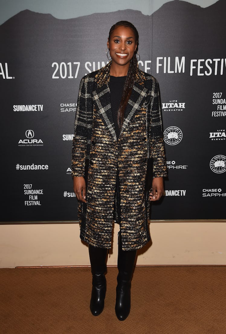 Issa wearing a long plaid coat, her hair up and hoop earrings at Sundance 