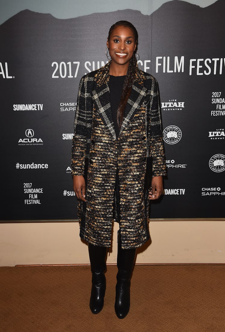 Issa wearing a long plaid coat, her hair up and hoop earrings at Sundance 