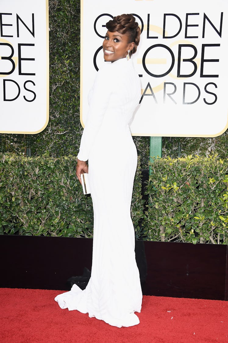 Issa wearing a long white gown with a matching white clutch at the Golden Globe Awards' red carpet