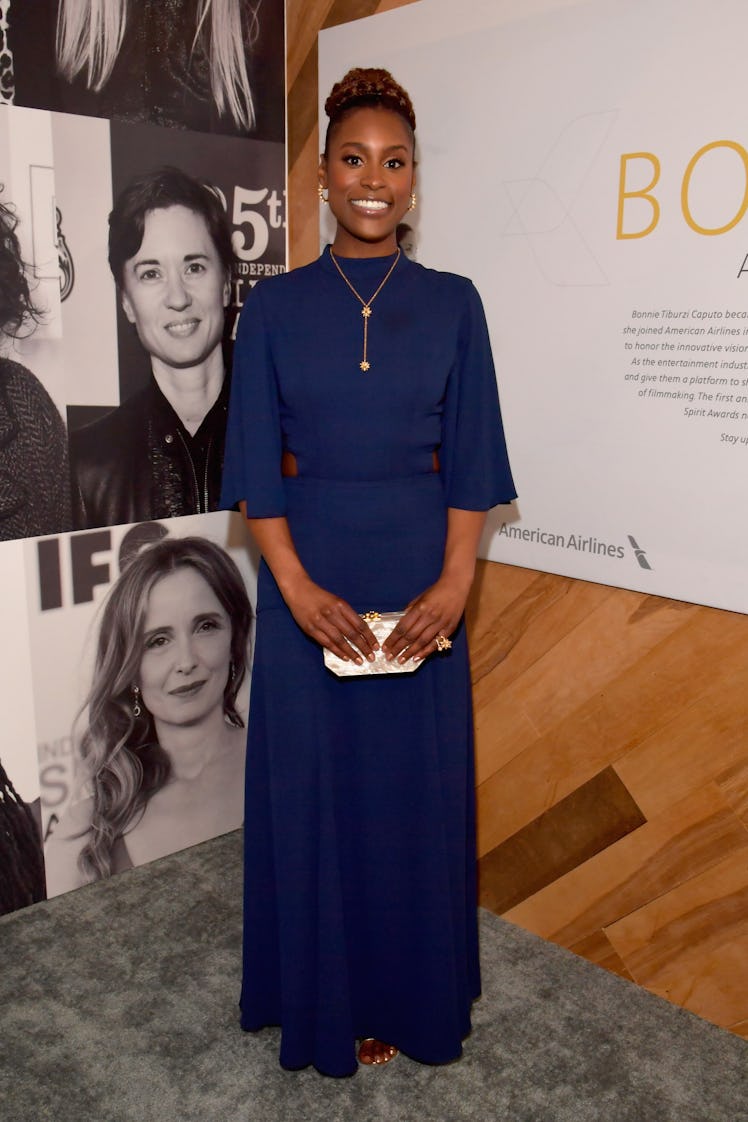 Issa in a long dark blue dress, a long thin necklace with two pendants on it and her hair up 
