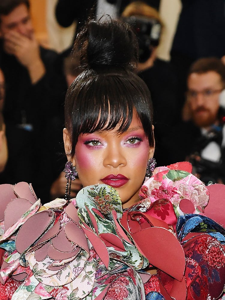 Rihanna wearing her hair in a sleek top knot and bangs, sporting a frosted magenta smoky eye at the ...