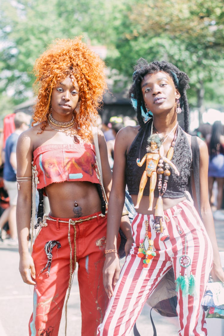 Two women at the Afropunk Festival: one in a red top and pants and the other is in striped pants and...