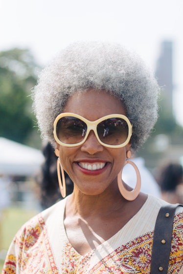 A woman with a grey afro, beige sunglasses and dangling large earrings smiling at the camera during ...