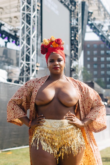 A woman wearing a floral headpiece, a brown caftan and gold skirt revealing her breasts at the Afrop...