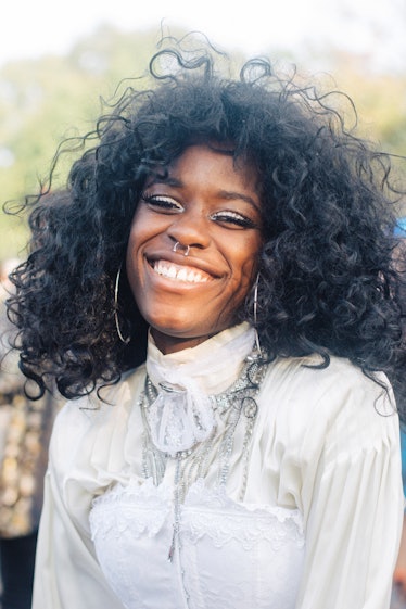 A woman with curly hair, shiny eye shadow and a septum piercing smiling at the Afropunk Festival 