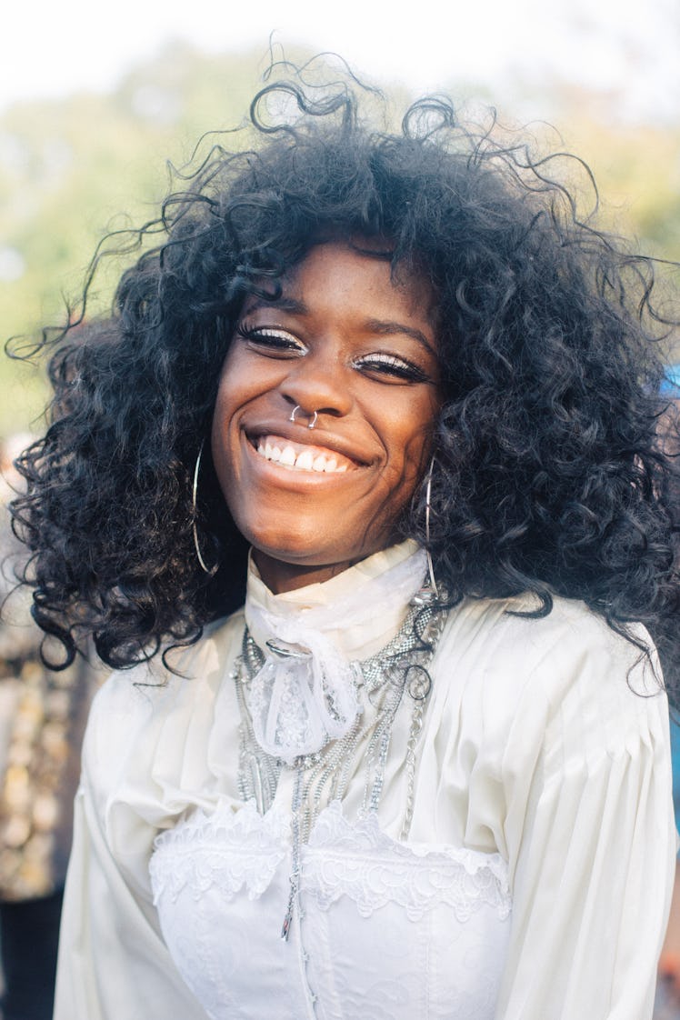 A woman with curly hair, shiny eye shadow and a septum piercing smiling at the Afropunk Festival 