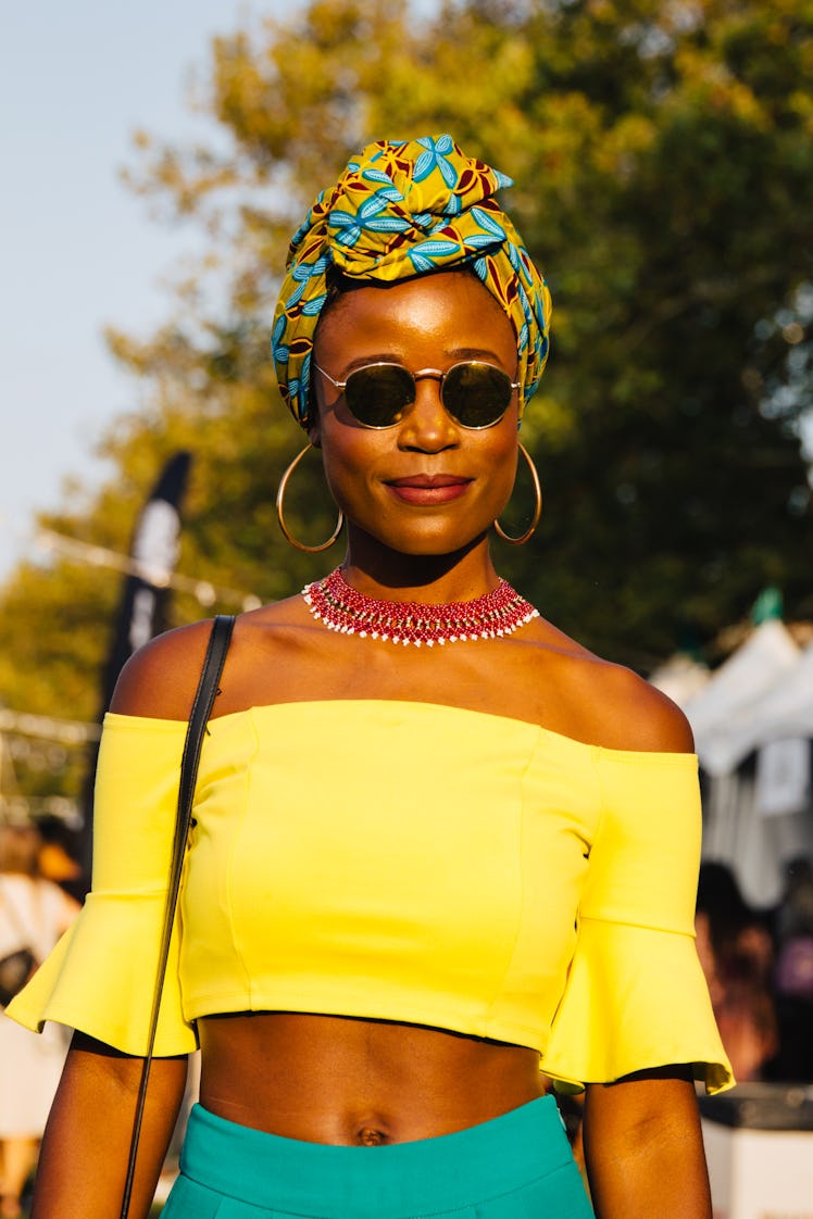A woman in a yellow off-the-shoulder crop top, and a yellow with turquoise headpiece at the Afropunk...
