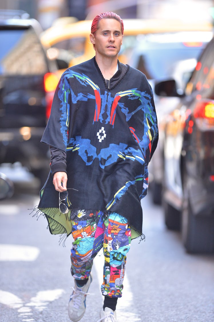 Jared Leto in a blue-navy-red poncho and multi-colored trousers and pink hair walking