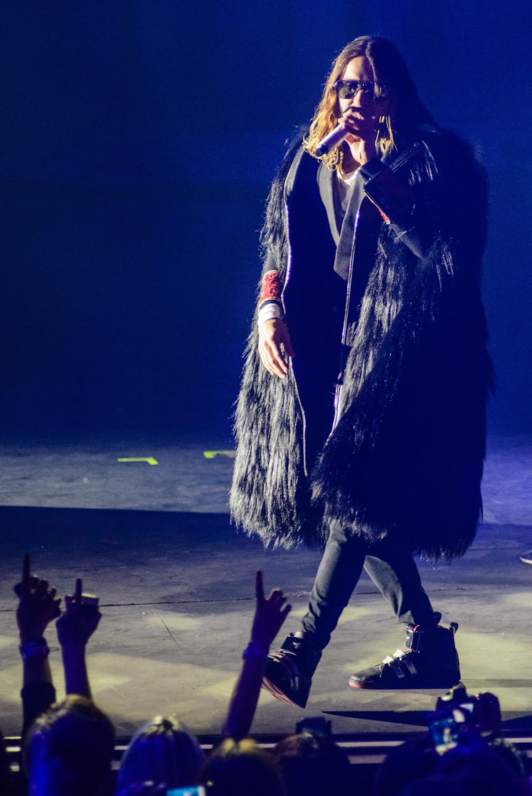 Jared Leto performing on stage while wearing a black fur poncho and black trousers