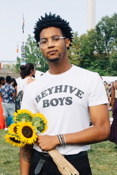 A man in a white t-shirt that says "beyhive boys" and sunflowers in his hand at Afropunk Festival 