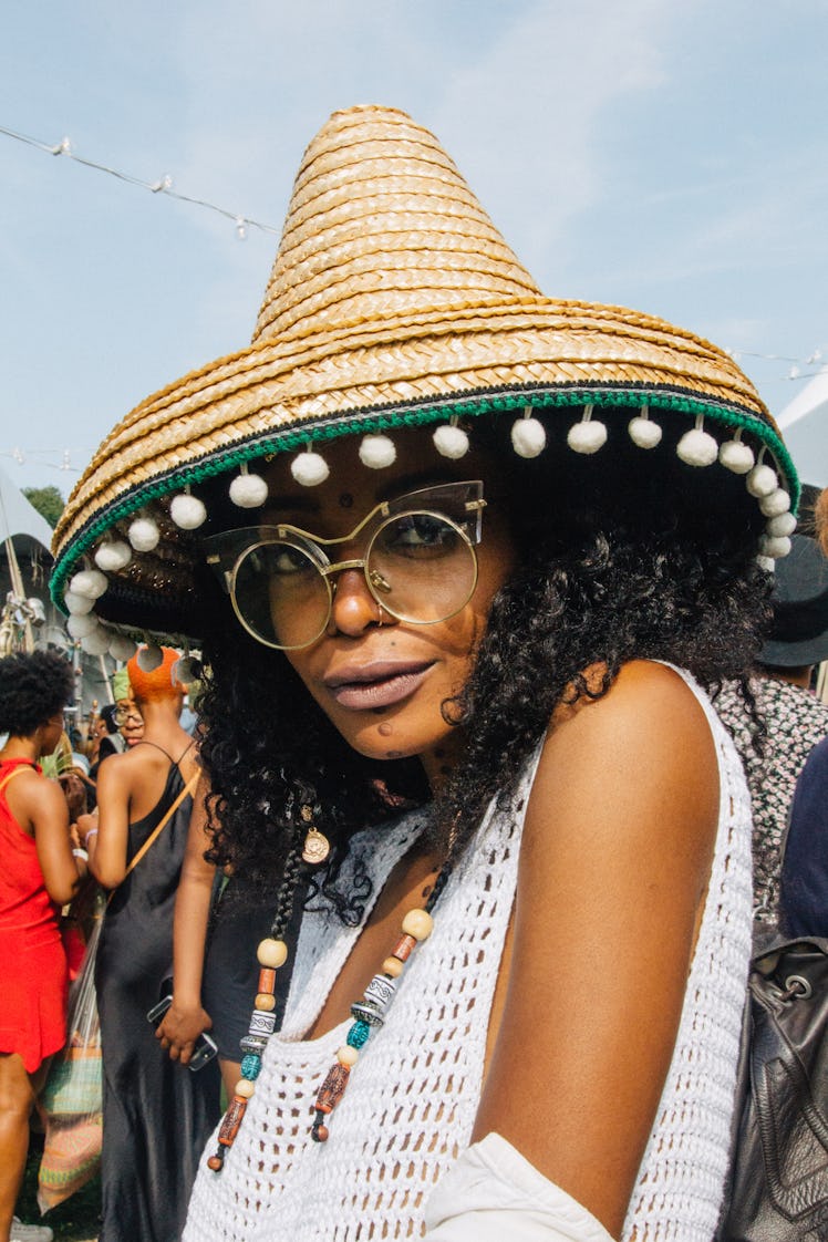 A woman wearing a sombrero and sunglasses with a white net tank top, at Afropunk Festival