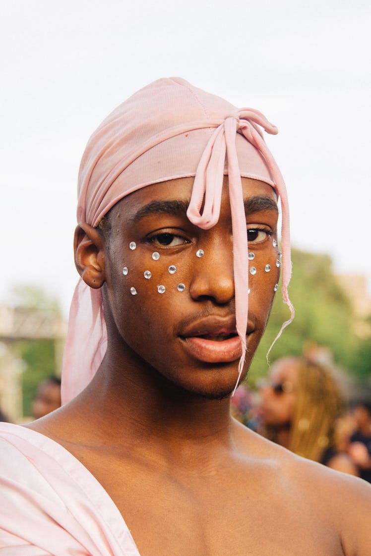 A man at Afropunk Festival with a light pink doo-rag and jewels on his face 