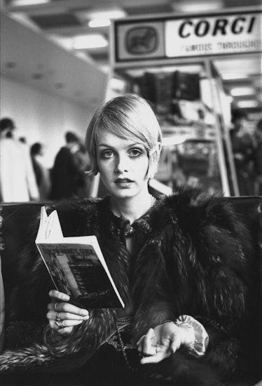 Twiggy reading a book, wearing a black furry coat with an iconic Pixie cut
