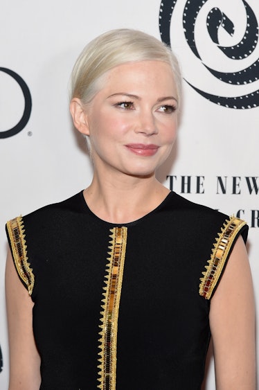 Michelle Williams wearing a blonde Pixie cut sleek and side-parted with a black dress and gold detai...