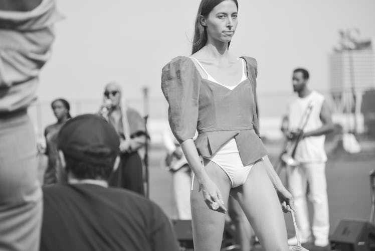 A black and white photo of a model in a top and a white bodysuit underneath walking the Maryam Nassi...