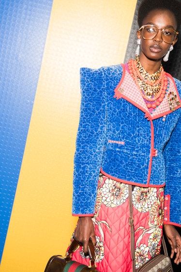 A model backstage at the Gucci SS18 show in Milan wearing a blue jacket, pink skirt and two Gucci ba...