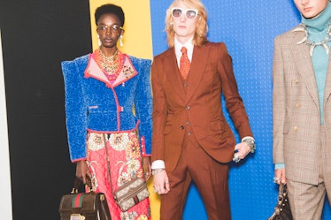 Two models backstage at the Gucci SS18 show in Milan: one in a brown suit and the other in a blue bl...