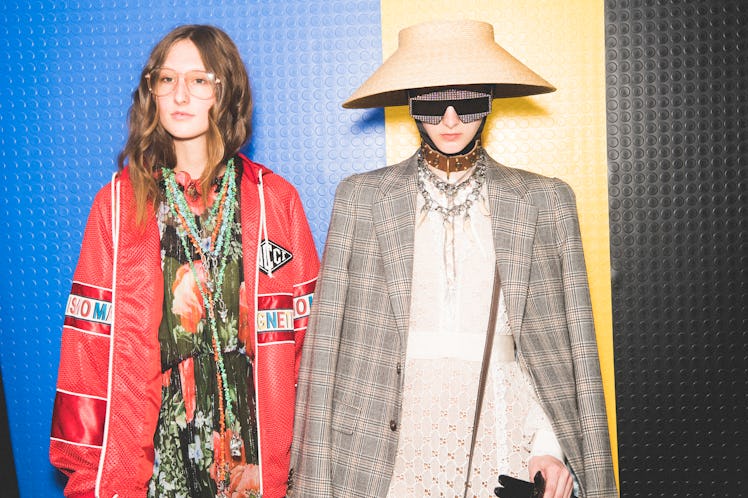 Two models backstage at the Gucci SS18 show wearing a dress with a red bomber jacket and a plaid bla...