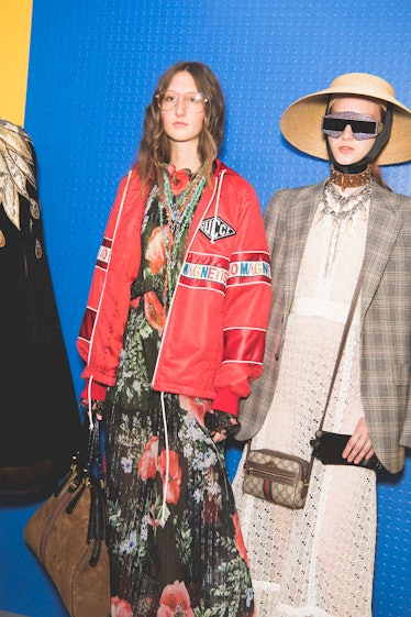 Two models backstage at the Gucci SS18 show wearing a dress with a red bomber jacket and a plaid bla...