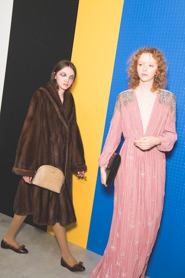 Two models backstage at the Gucci SS18 show, one in a long flowy pink gown and the other in a fur co...