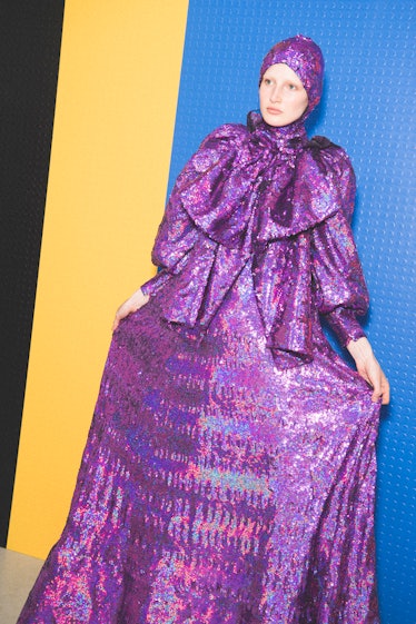 A model posing in a shimmery purple dress that has a matching head piece 