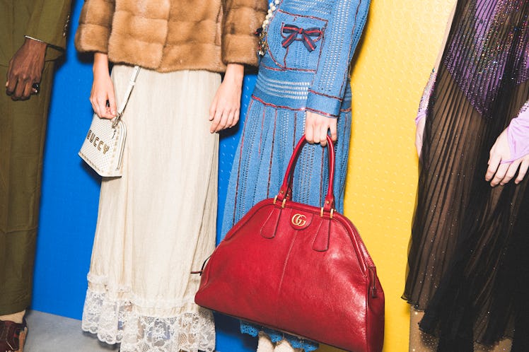 Two models standing backstage at the Gucci SS18 show, one is holding a large red tote bag 