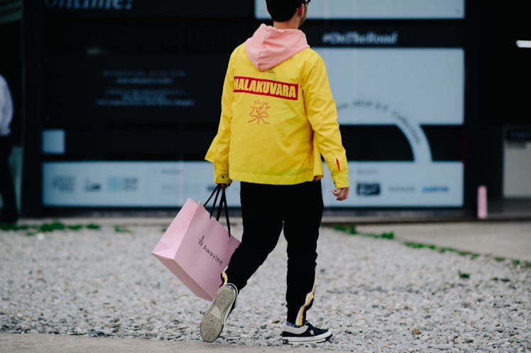 Aman walking while wearing a yellow jacket and carrying a pink bag