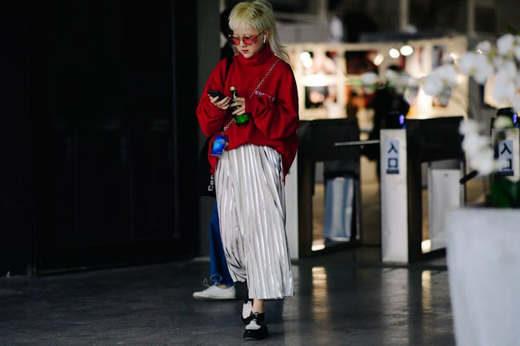 A blonde woman walking while wearing white baggy pants and a red sweater