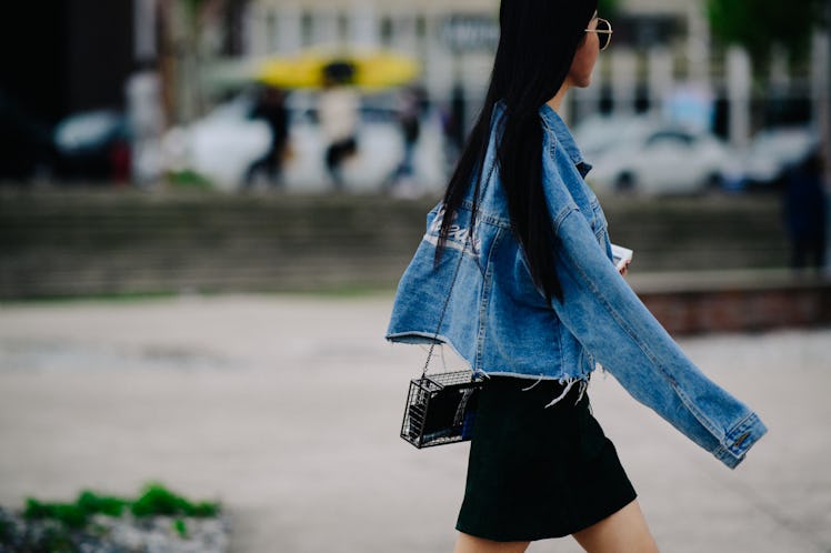 A woman walking while wearing a black mini dress and a denim blue jacket