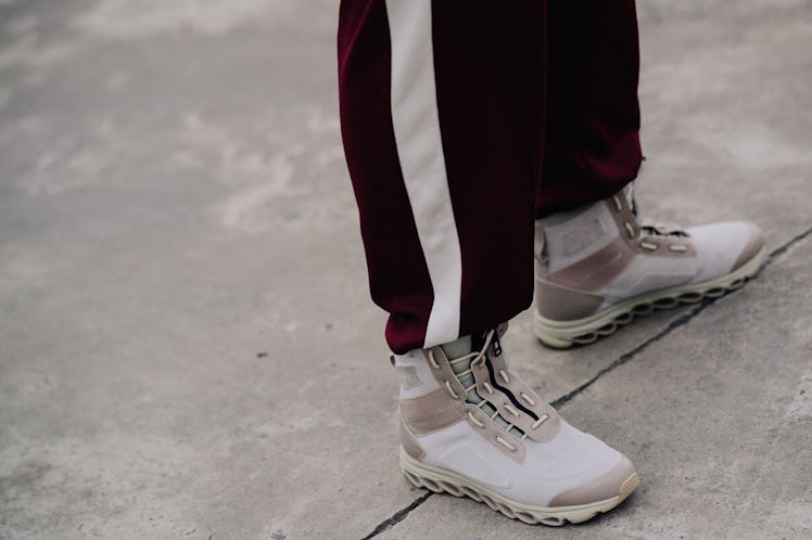 A man standing while wearing burgundy and white pants and white shoes