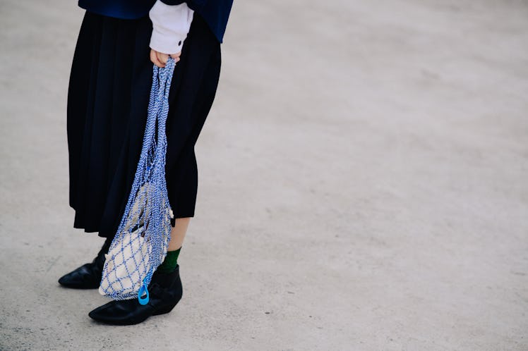 Legs of a woman that is wearing a black dress, black shoes, and is holding a blue netted bag