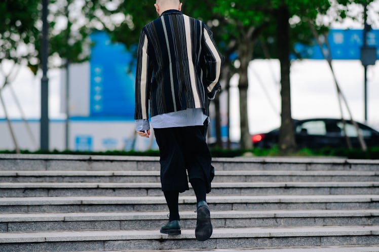 A man walking while wearing black baggy pants and a black blazer