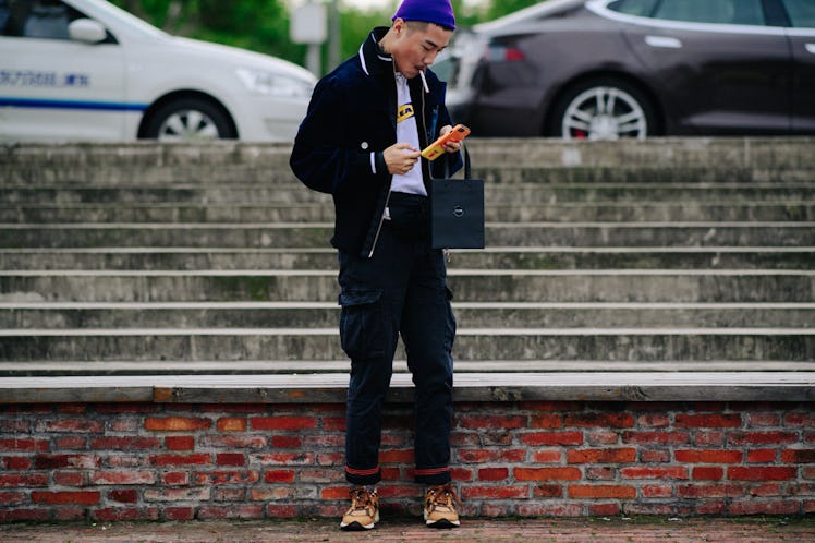 A boy standing while wearing a black blazer, black pants, and a blue cap