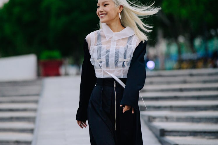 A blonde woman walking while wearing a black skirt and a white top