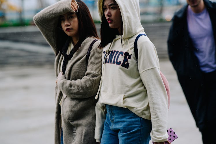 Two girls walking, one is wearing a white hoodie and the other one is wearing a grey coat