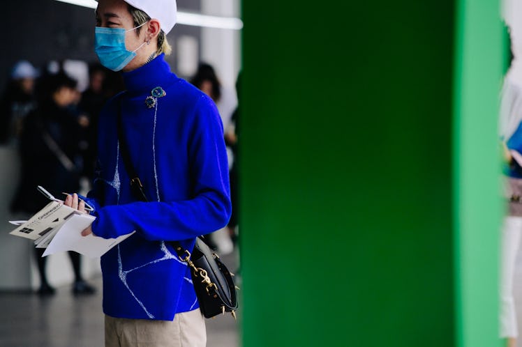 A man standing with a mask on his face while wearing a blue jacket