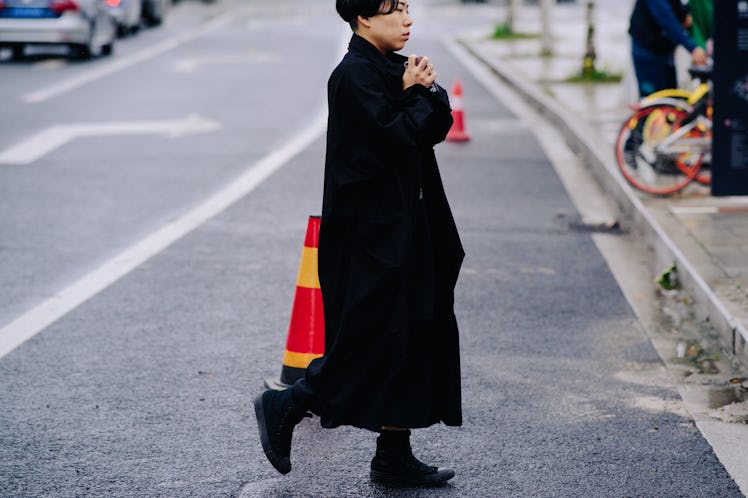 A woman crossing a street while wearing a black coat