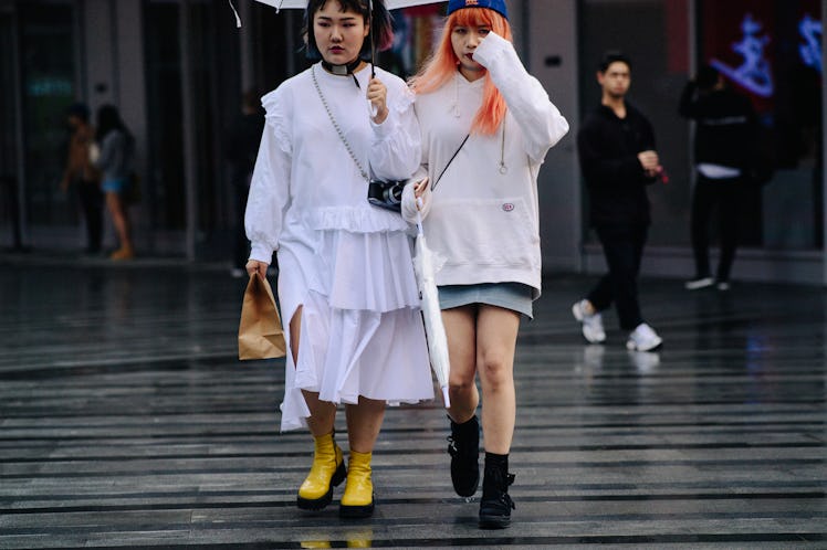 Two girls walking under an umbrella, one is wearing a white dress and the other one is wearing a whi...