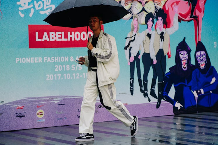 A man walking under a black umbrella while wearing a white tracksuit top and pants