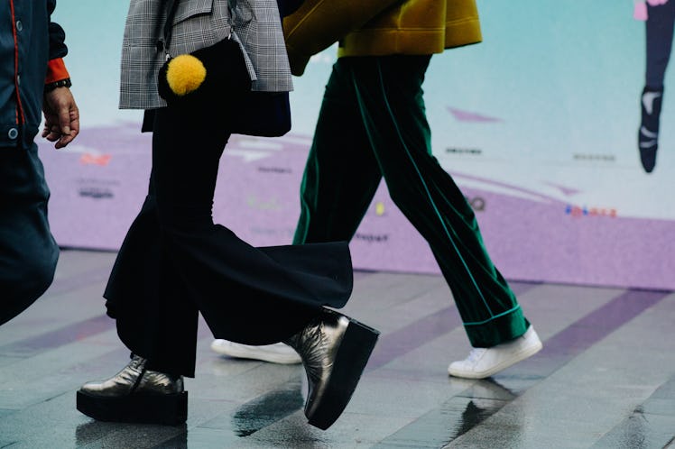 Legs of two women walking while wearing black and green baggy pants