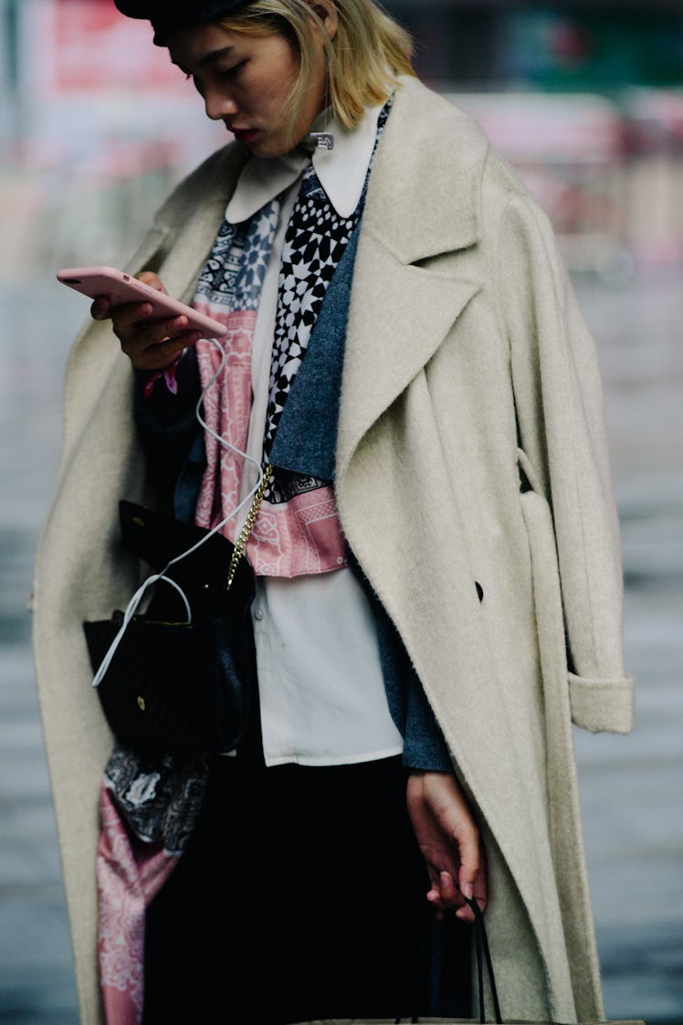 A woman using her mobile phone while wearing a white coat