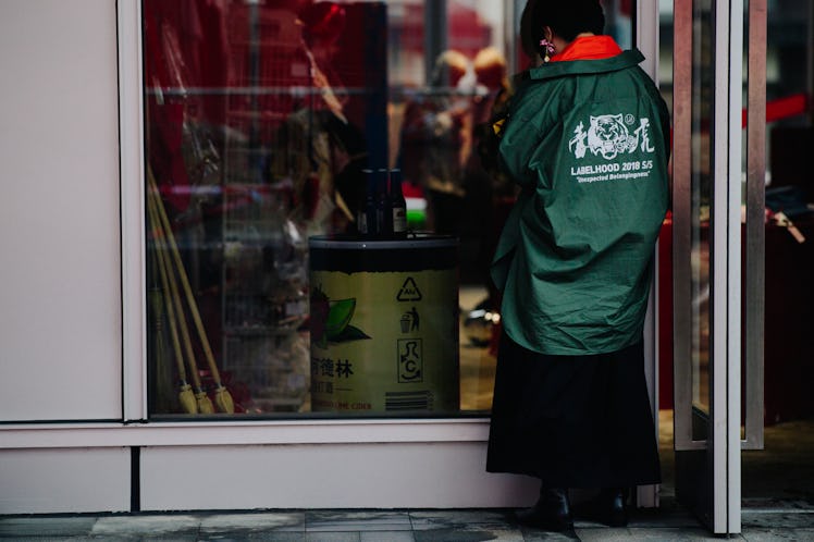 A woman looking at a shop window while wearing a green jacket 