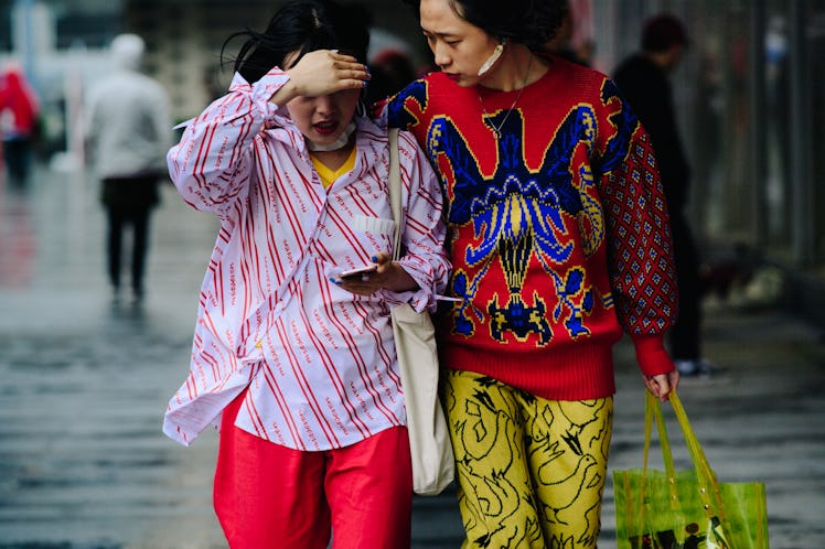 Two women walking together, one is wearing a white shirt and the other is wearing a red and blue swe...