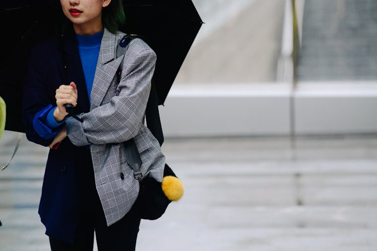 A woman holding a black umbrella while standing in a black and grey blazer over a blue shirt