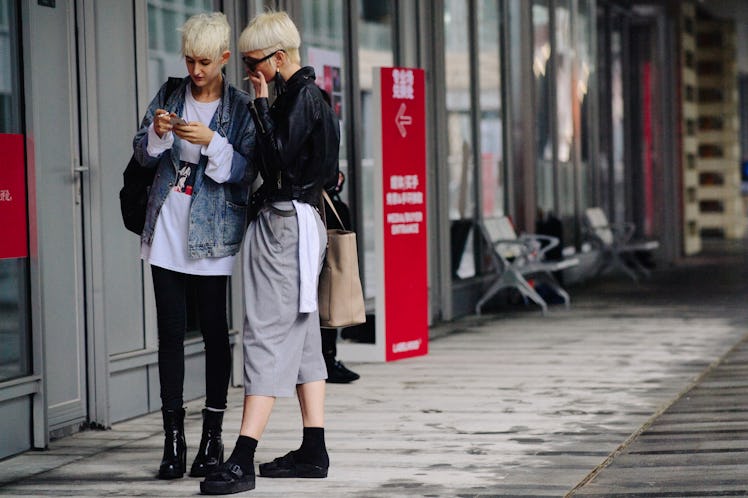 Two blonde short-haired ladies standing next to each other on a street
